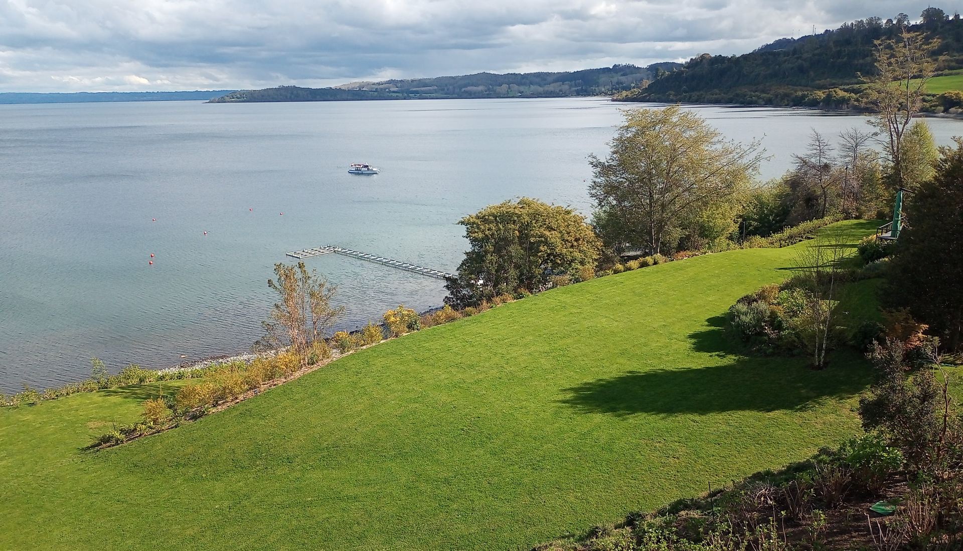 Jardín terminado en pendiente hacia el lago, con muelle al fondo, en Imahue, Futrono